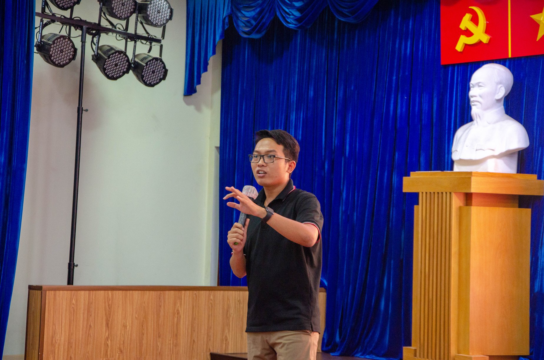 A person standing in front of a stage holding a microphone

AI-generated content may be incorrect.